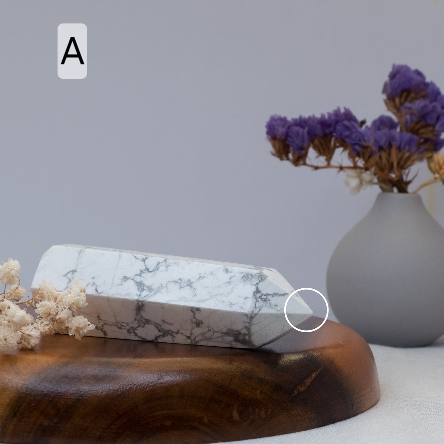 Howlite tower on a wooden surface with a vase of purple flowers in the background.