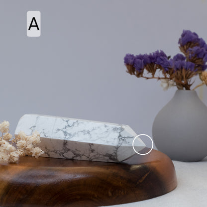 Howlite tower on a wooden surface with a vase of purple flowers in the background.