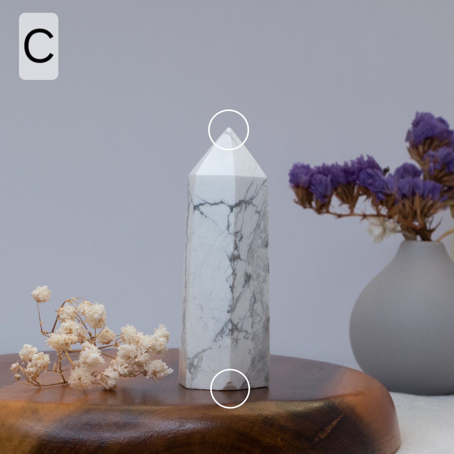 Howlite crystal tower on a wooden surface with flowers and a vase in the background.