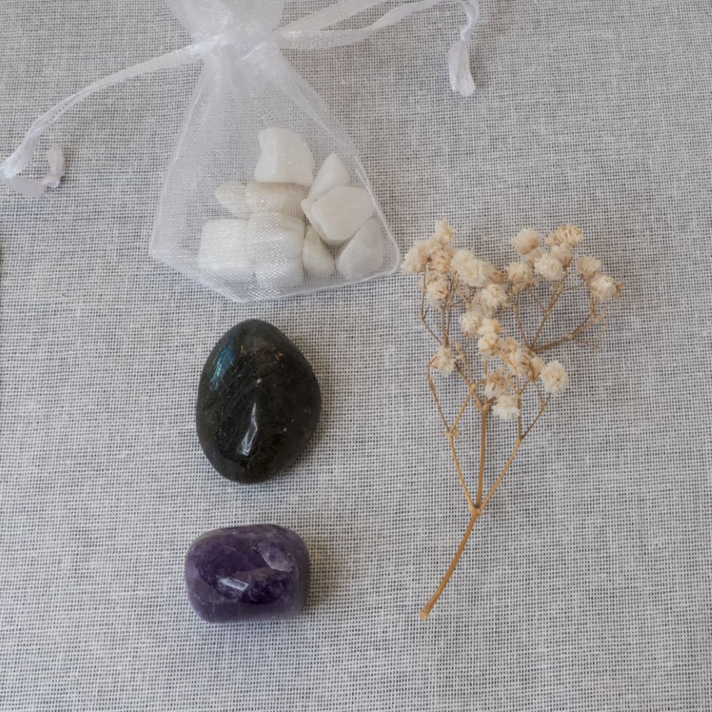 Two stones, a small bag of white moonstone, and a sprig of dried flowers on a textured surface.