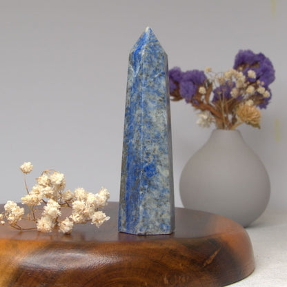 lapis lazuli obelisk on a wooden surface with a vase of flowers in the background