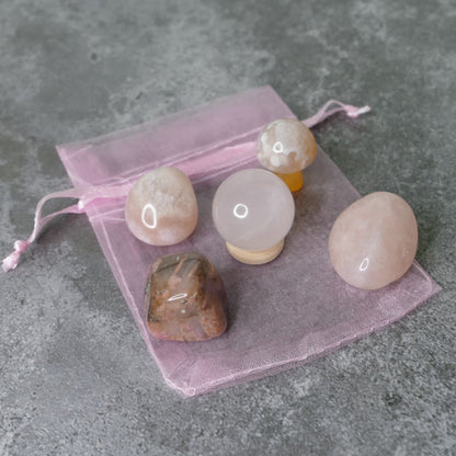 Set of polished stones on a pink drawstring bag against a gray concrete background