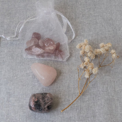 a rose quartz tumblestone, a rhodonite tumble stone and some strawberry chips , a branch of dried flowers on a textured fabric background