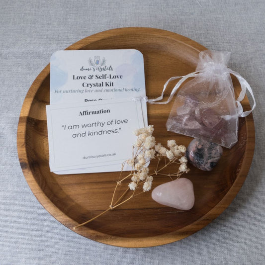 Love & Self-Love Crystal Kit with rose quartz, rhodonite and strawberry quartz, card, and flowers on a wooden tray.