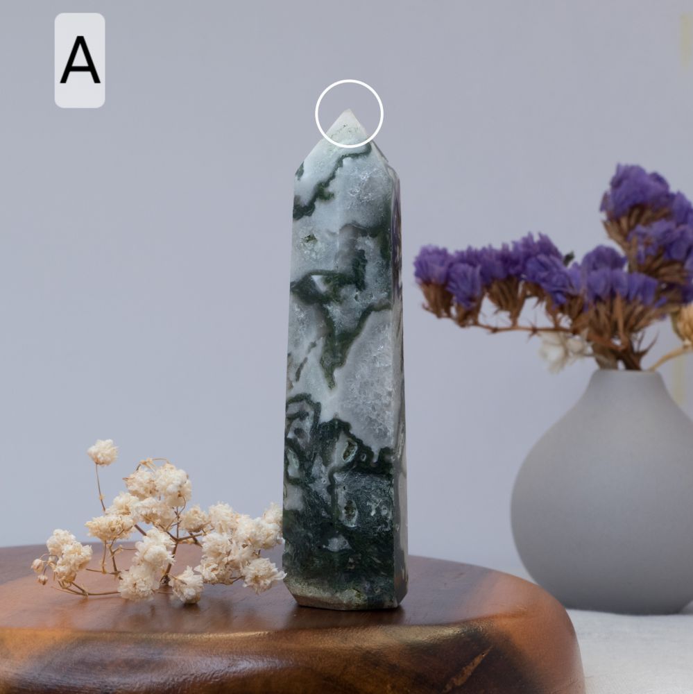 moss agate tower on a wooden surface, with a vase of purple flowers in the background.