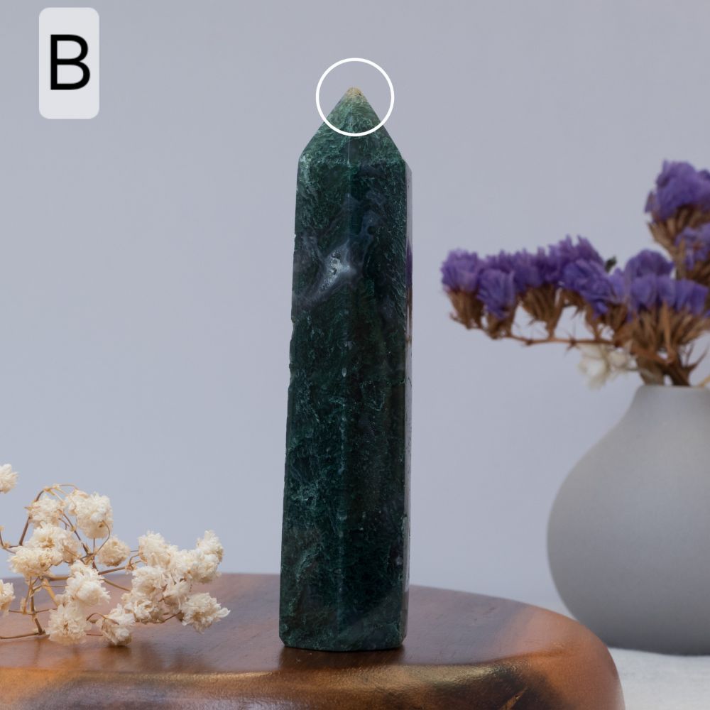 moss agate tower  on a wooden surface with a vase of purple flowers in the background.