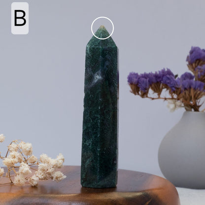 moss agate tower  on a wooden surface with a vase of purple flowers in the background.