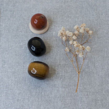 red jasper, black obsidian, tiger's eye and a small branch of dried flowers on a textured gray surface