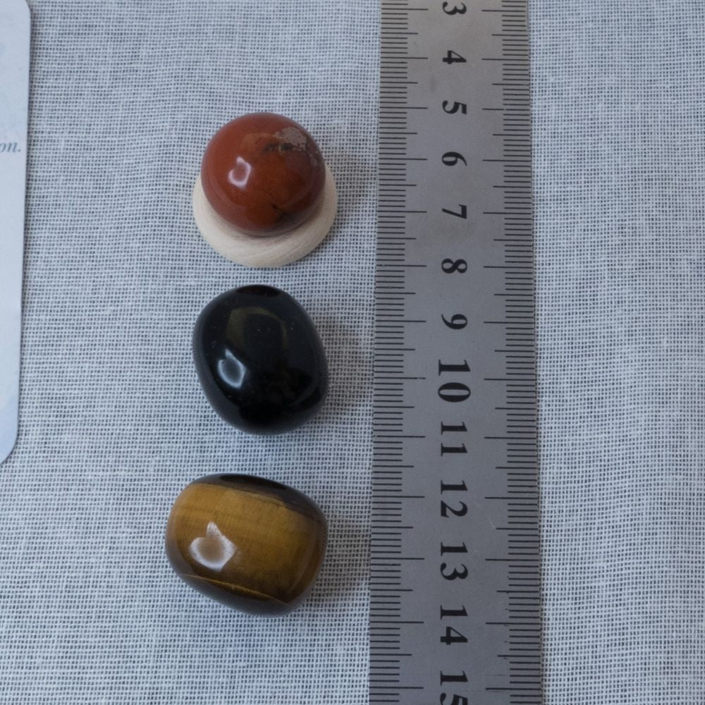 Three stones of different colors (red, black, brown) on a textured surface with a ruler for scale.