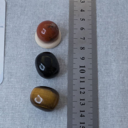Three stones of different colors (red, black, brown) on a textured surface with a ruler for scale.