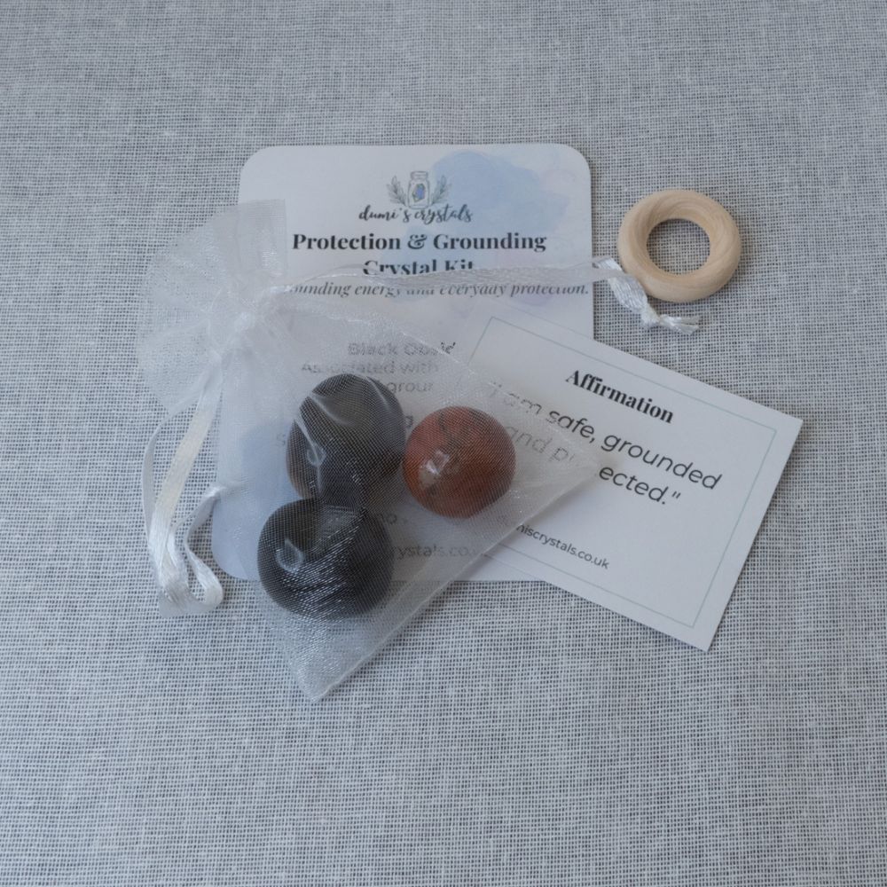 red jasper mini sphere, tiger's eye and black obsidian tumbles in bag with cards on a textured surface