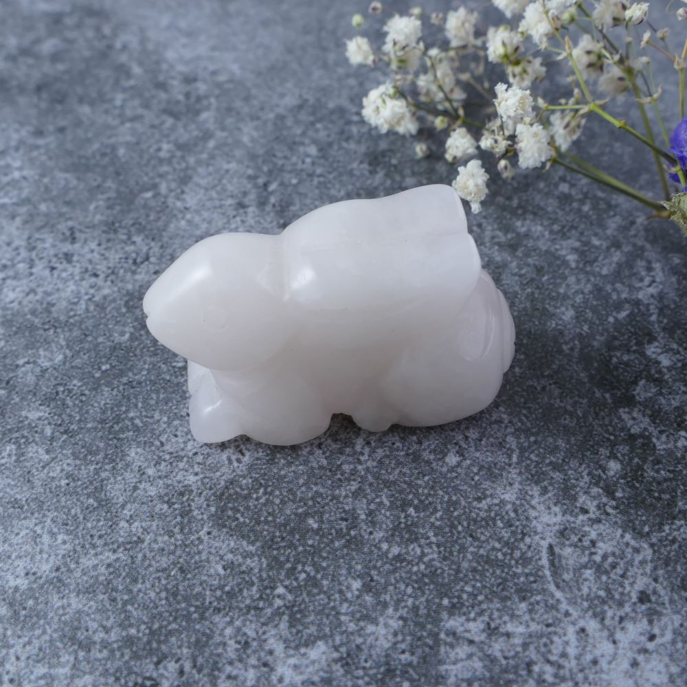 Dumi's Crystals | Rose Quartz Bunny Carving (Gentle Spirit):  A close-up of a Rose Quartz Crystal Bunny Carving, radiating a soft, light pink hue. Hand-crafted with love, this gentle spirit promotes self-love, forgiveness, & positive energy. Embrace inner peace with Dumi's Crystals (ethically sourced).