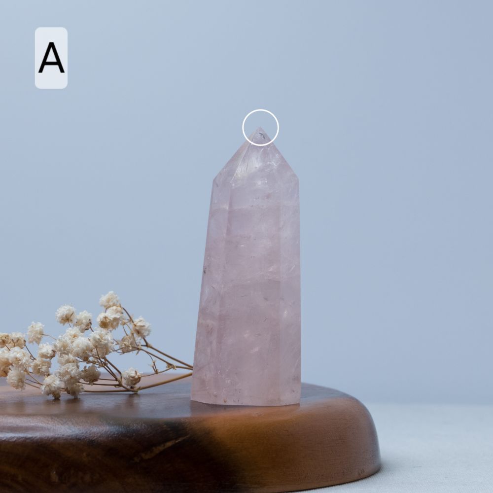 Rose quartz crystal tower on a wooden base with dried flowers against a light blue background