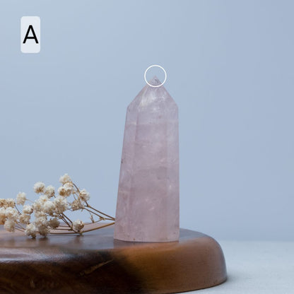 Rose quartz crystal tower on a wooden base with dried flowers against a light blue background