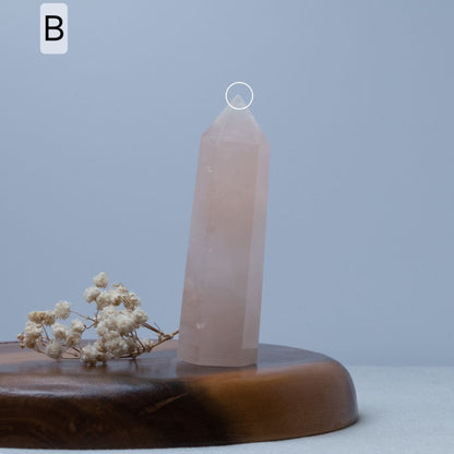 Rose quartz crystal tower on a wooden base with dried flowers against a light blue background