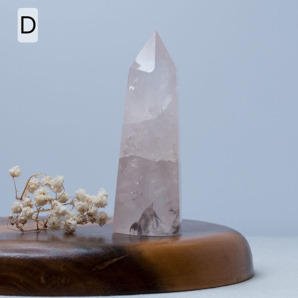 Crystal obelisk on a wooden base with dried flowers against a light blue background