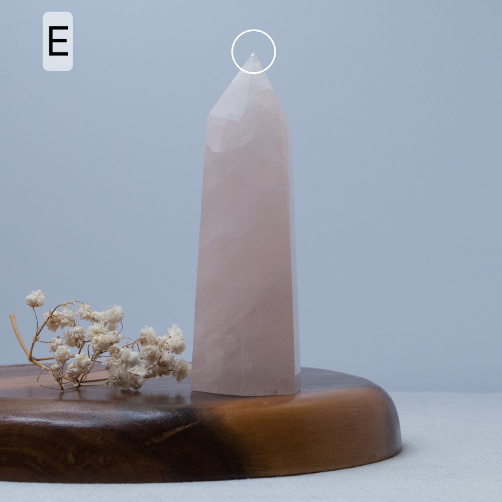 rose quartz Crystal obelisk on a wooden base with dried flowers against a light blue background