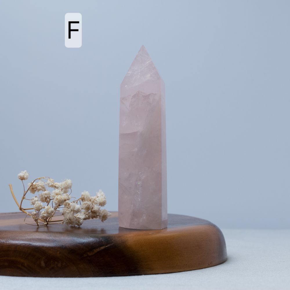 Rose quartz crystal tower on a wooden base with dried flowers against a light blue background