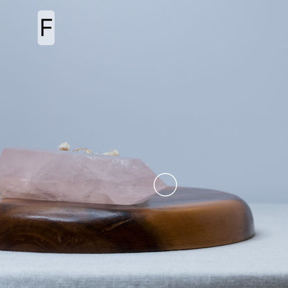 Rose quartz crystal on a wooden stand with a gray background