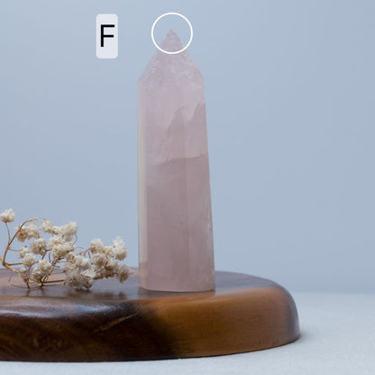 Rose quartz crystal on a wooden stand with dried flowers against a light blue background