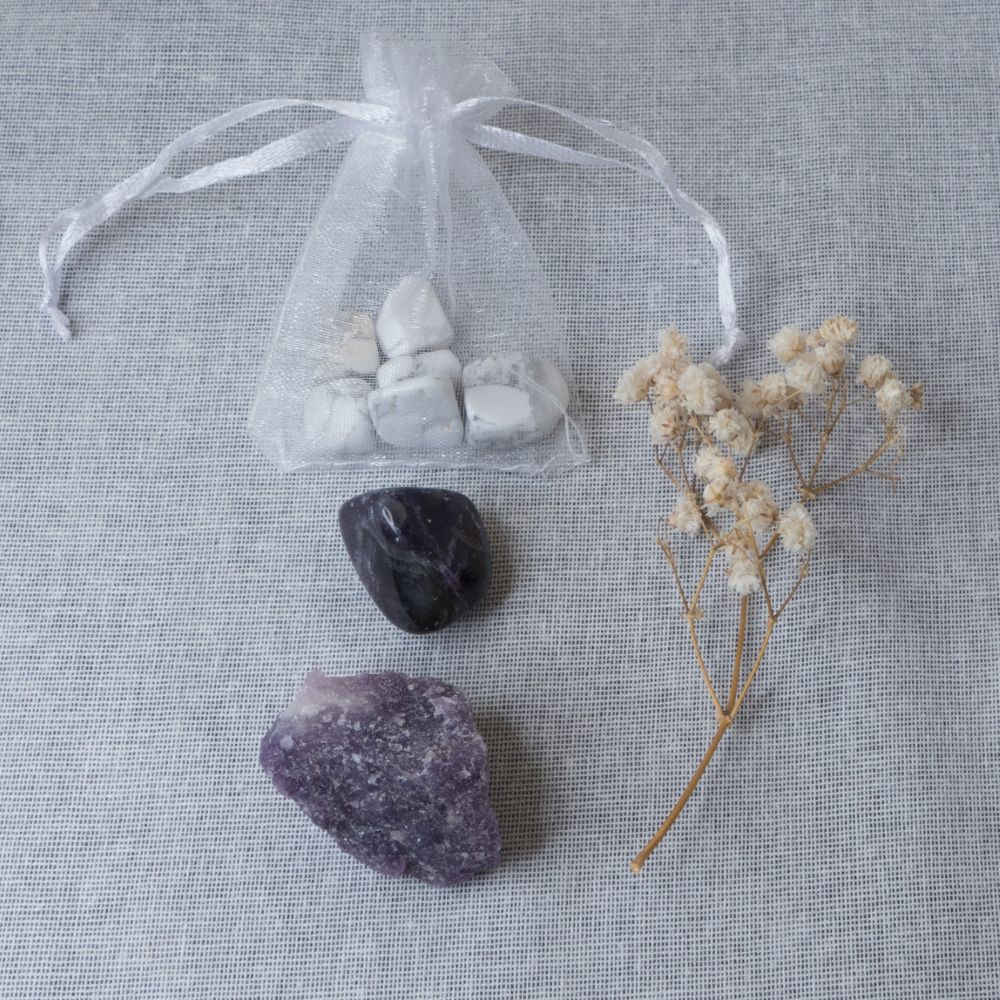 howlite chips, amethyst tumble stone and lepidolite rough stone on a white surface with a clear bag and dried flowers.