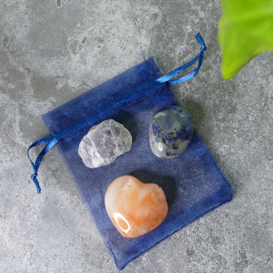 Three crystals fluorite, polished sodalite and a carnelian heart on a blue drawstring bag against a gray concrete background