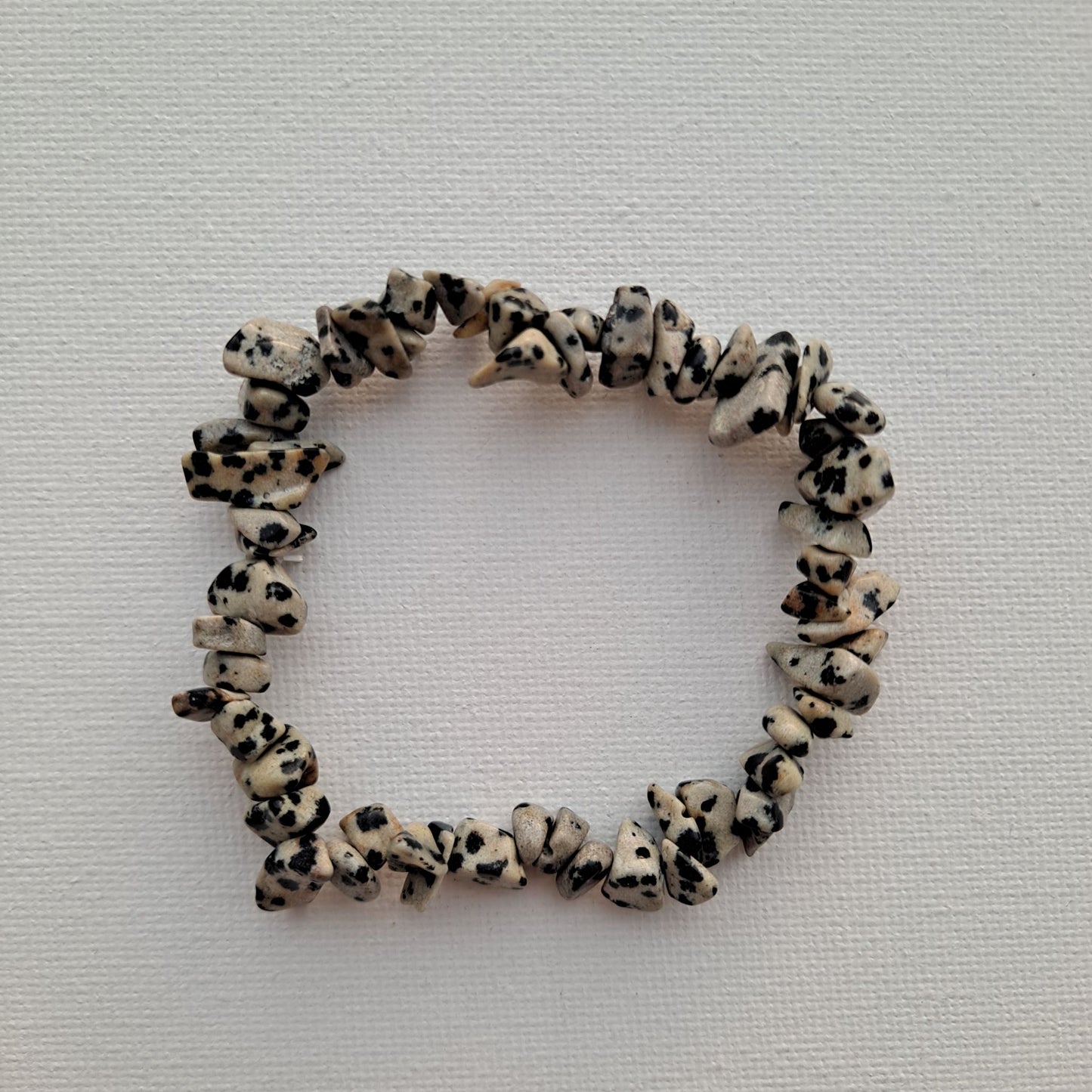  Dumi's Crystals | Dalmatian Jasper Chip Stretch Bracelet (7 Inch) | Close-up of a handcrafted bracelet featuring genuine Dalmatian Jasper chips with their characteristic black spots on a creamy beige background. Dalmatian Jasper is a unique type of Jasper, known for its playful energy and grounding protection.