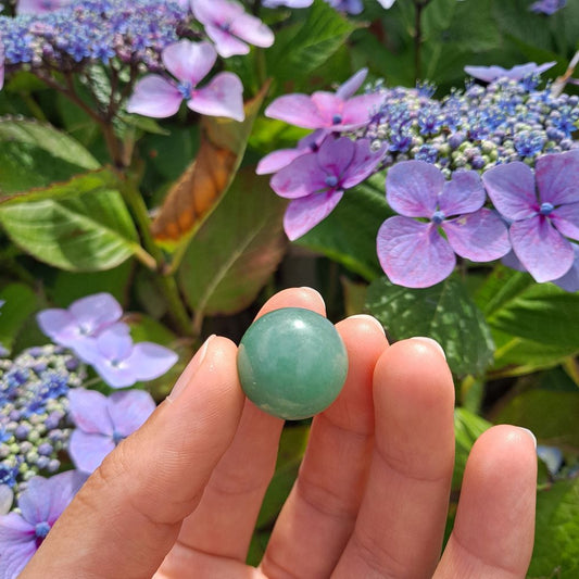 Dumi's Crystals | Green Aventurine Mini Sphere (20mm) | A close-up view of a captivating Green Aventurine Mini Sphere, showcasing its vibrant green hues and glistening sheen. This 20mm sphere is believed to promote peace, love, abundance, and emotional healing. It's also thought to attract good fortune and encourage optimism.