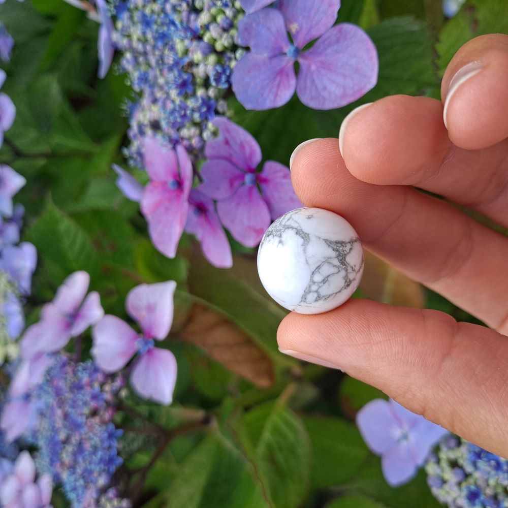  Dumi's Crystals | Howlite Mini Sphere (20mm) | A close-up view of a captivating Howlite Mini Sphere, showcasing its smooth, white surface with subtle marbling. This 20mm sphere, known as the "stone of calmness," is believed to promote peace, relaxation, and mental clarity. It's also thought to improve communication and foster deeper connections.