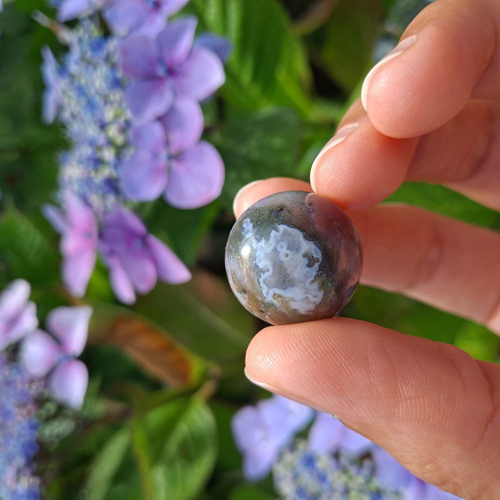 Dumi's Crystals | Indian Agate Mini Sphere (20mm) | A close-up view of a captivating Indian Agate Mini Sphere, showcasing its unique bands of color and smooth surface. This 20mm sphere is believed to promote balance, emotional well-being, and a deeper connection with the Earth. It's also thought to alleviate stress and enhance intuition.