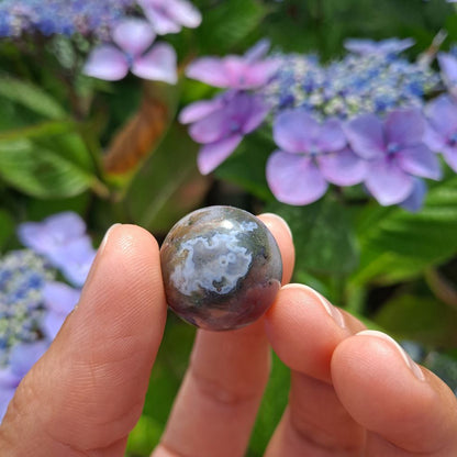 Dumi's Crystals | Indian Agate Mini Sphere (20mm) | A close-up view of a captivating Indian Agate Mini Sphere, showcasing its unique bands of color and smooth surface. This 20mm sphere is believed to promote balance, emotional well-being, and a deeper connection with the Earth. It's also thought to alleviate stress and enhance intuition.