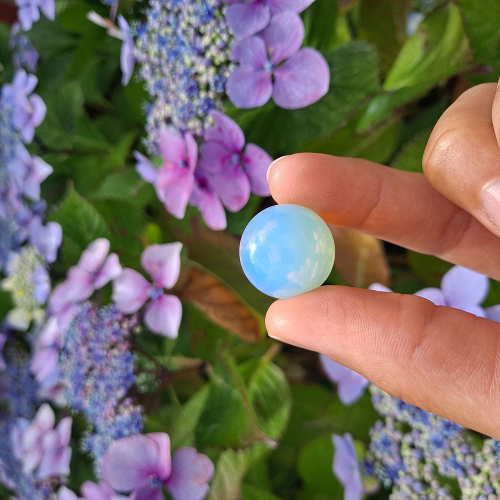 Dumi's Crystals | Opalite Mini Sphere (20mm) | A close-up view of a captivating Opalite Mini Sphere, showcasing its vibrant play of color and smooth surface. This 20mm, man-made stone is believed to promote peace, serenity, and personal growth. It's also thought to enhance intuition and spiritual connection.